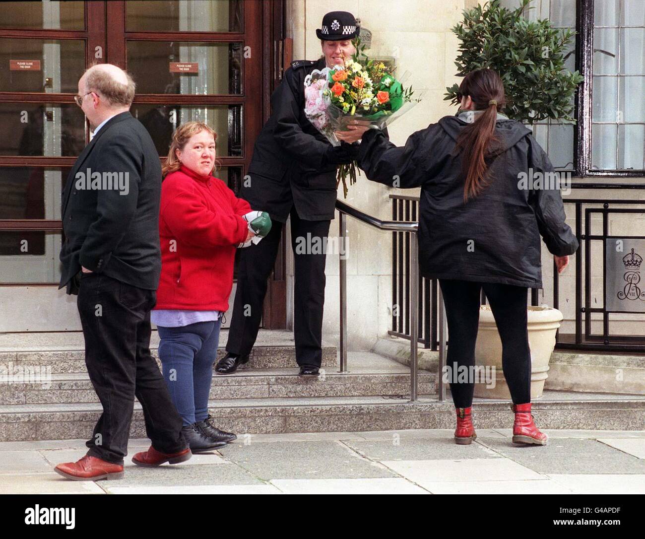 Un wellwisher entrega flores a una mujer de policía de pie guardia fuera de la entrada al hospital Rey Eduardo VIII en Londres esta mañana (lunes), donde la Reina Madre se está recuperando después de una operación exitosa de cadera anoche. La niña de 97 años se fracturó la cadera izquierda cuando cayó ayer en Sandringham. Ver PA Story Royal madre. Foto de Neil Munns/PA. Foto de stock