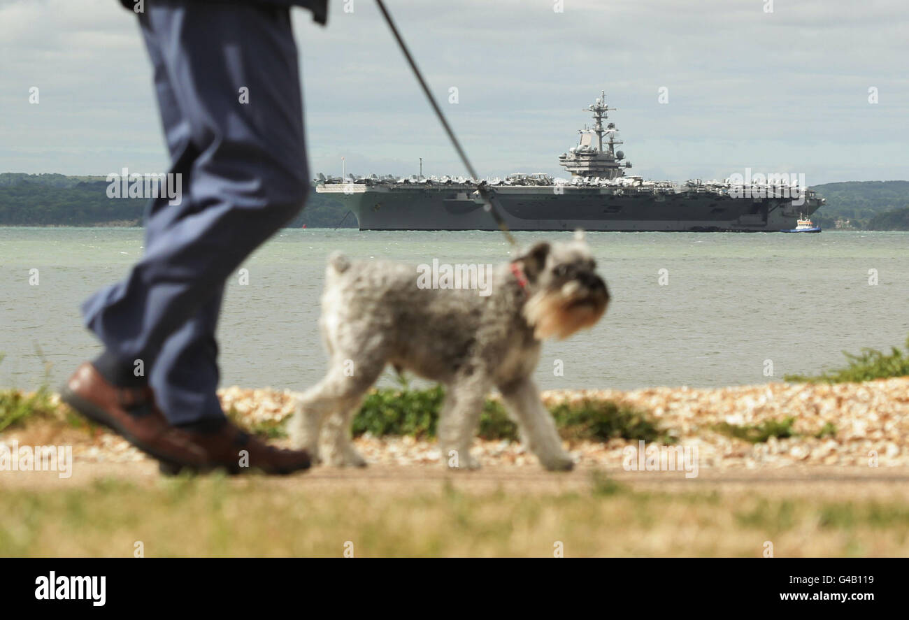 Un perro es caminado por la Marina de los Estados Unidos Nimitz super carrier de la clase USS George H.W. Bush en Stokes Bay, frente a la costa de Portsmouth. Foto de stock