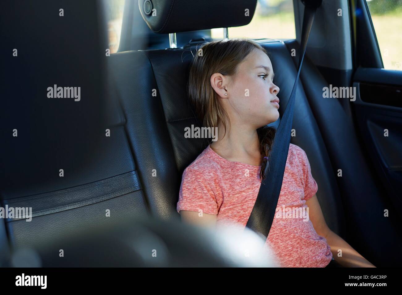 Modelo liberado. Chica en el asiento de atrás del coche usando el cinturón de seguridad. Foto de stock