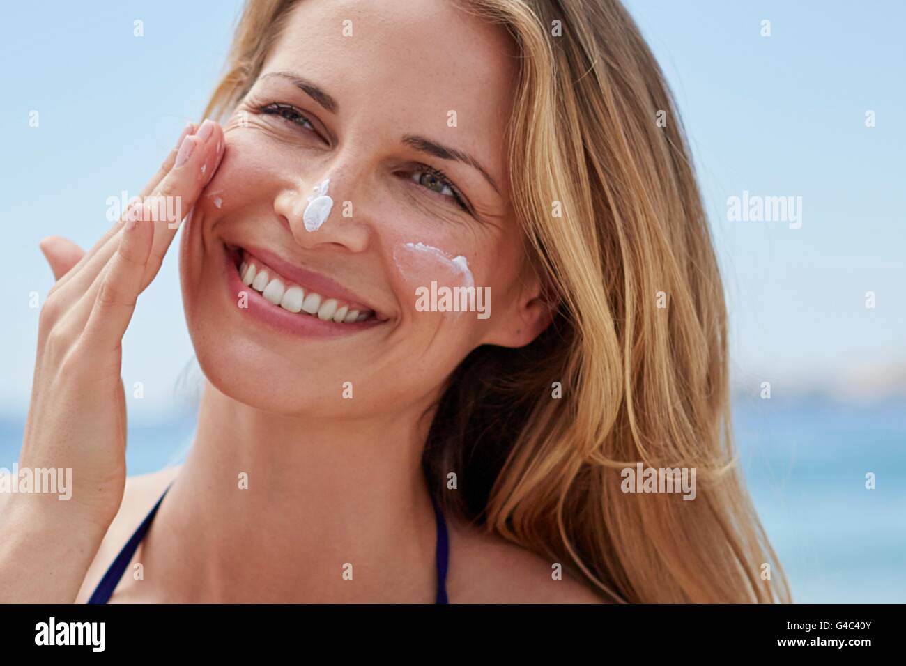 Modelo liberado. Mujer joven de aplicar crema para el sol en su cara. Foto de stock