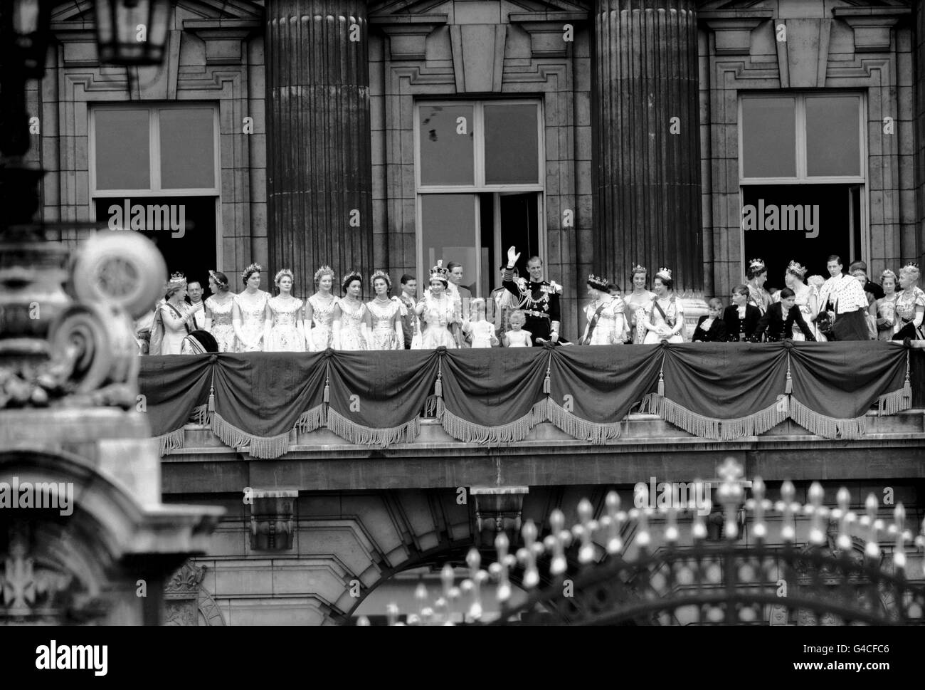 A la izquierda de la Reina están: La Princesa Real y las Seis Mapeas de Coronación de la Reina; Lady Rosemary Spencer-Churchill; Lady Moira Hamilton; Lady Jane Heathcote-Drummond-Willoughby; Lady Anne Coke; lady Mary Baillie-Hamilton; y Lady Jane Vane-Tempest-Stewart. A la derecha del Duque de Edimburgo están la Reina Isabel la Reina Madre; la Princesa Margarita; el Príncipe Richard de Gloucester; el Príncipe Guillermo de Gloucester; la Duquesa de Kent; el Príncipe Miguel de Kent; la Princesa Alexandra de Kent; el Duque de Kent; y la extrema derecha, la Princesa Alice de Athlone. Foto de stock