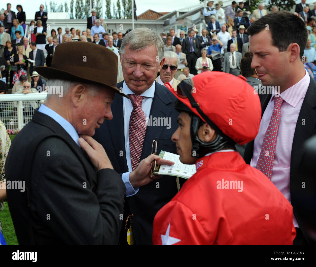 Sir Alex Ferguson escucha como el entrenador Barry Hills (izquierda) y su hijo Charlie (derecha) hablar con el jinete Silvestre De Sousa que estaba montando a caballo Sir Alex enfrenta el problema en el grupo sinfónico Stakes durante el Ebor Festival 2011 en el hipódromo de York. Foto de stock