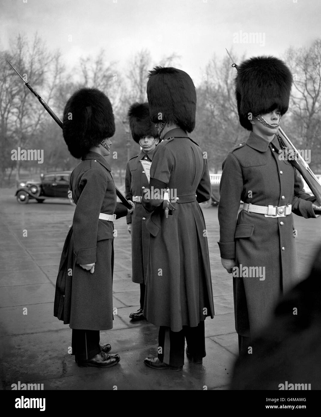 Un oficial de la Guardia en el Palacio de Buckingham, con una banda de brazo negro, inspecciona un guardia del Palacio y comprueba sus funciones, tras la muerte del rey Jorge VI Foto de stock