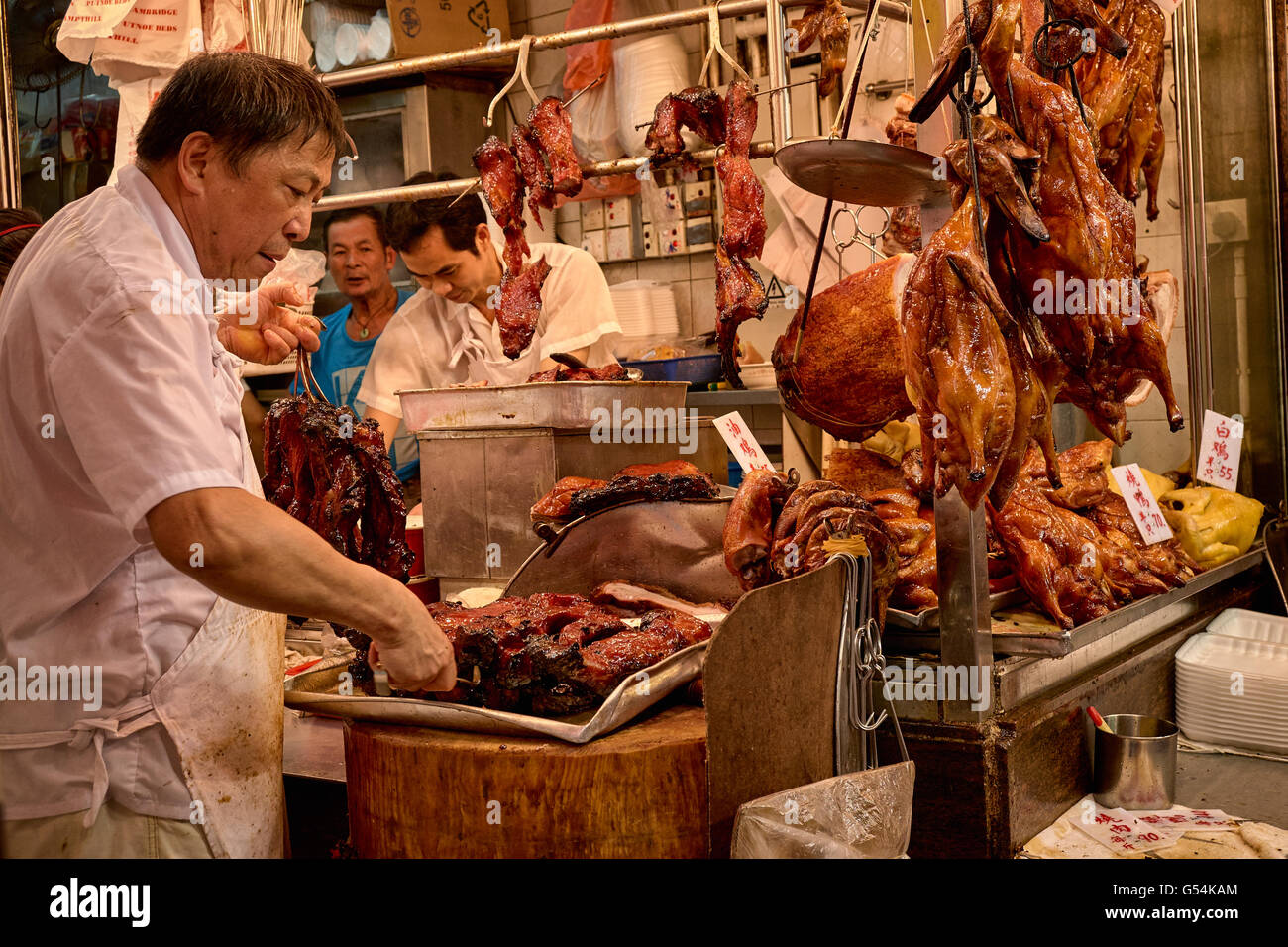 Un carnicero prepara algunos cha-siu en una tienda de alimentos cocinados en Shanghai Street en Yau Ma Tei, Hong Kong. Foto de stock