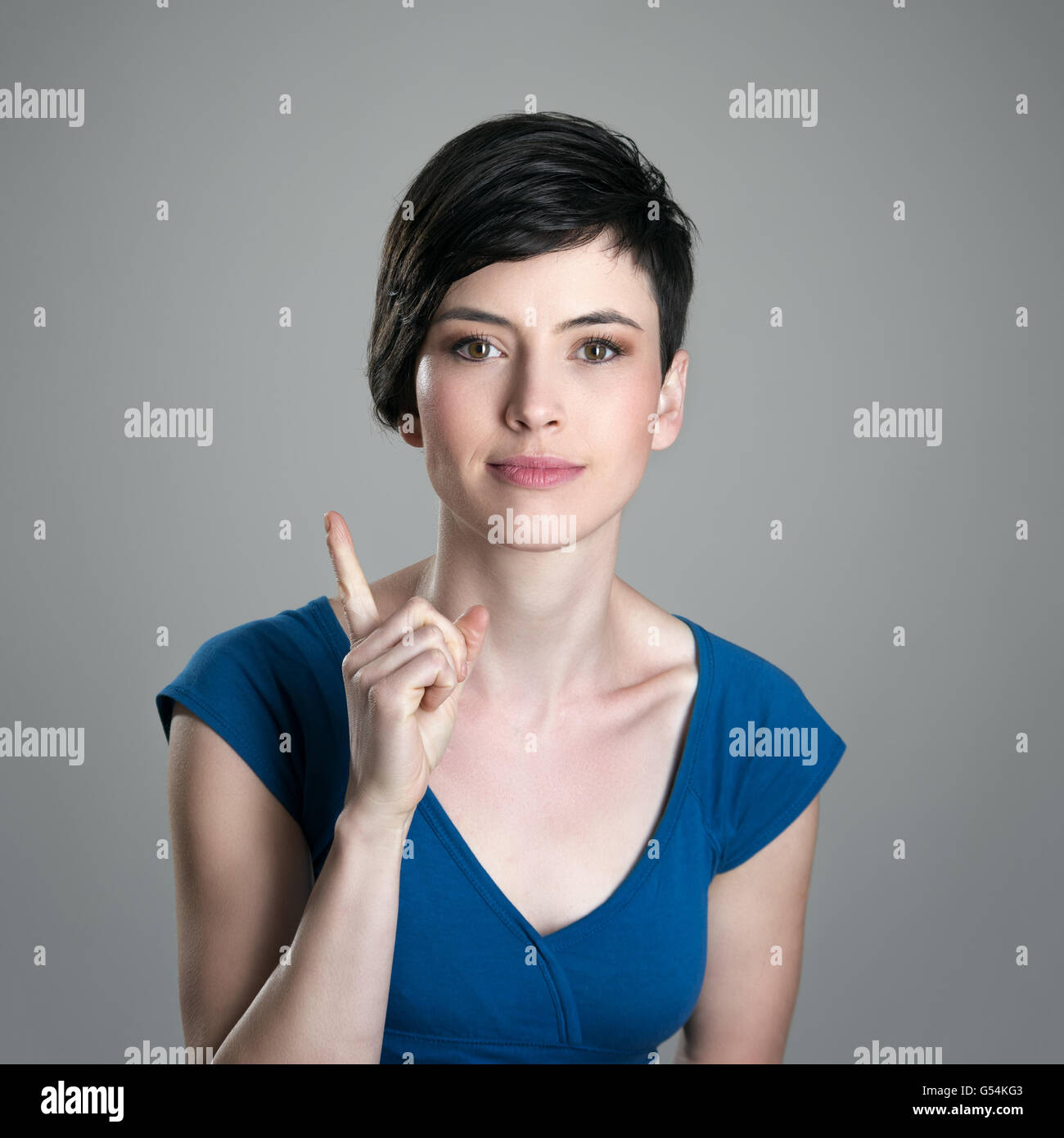 Sonriente Joven Cabello Corto Mujer Reganos Dedo Mirando A La Camara Sobre Fondo Gris Studio Fotografia De Stock Alamy