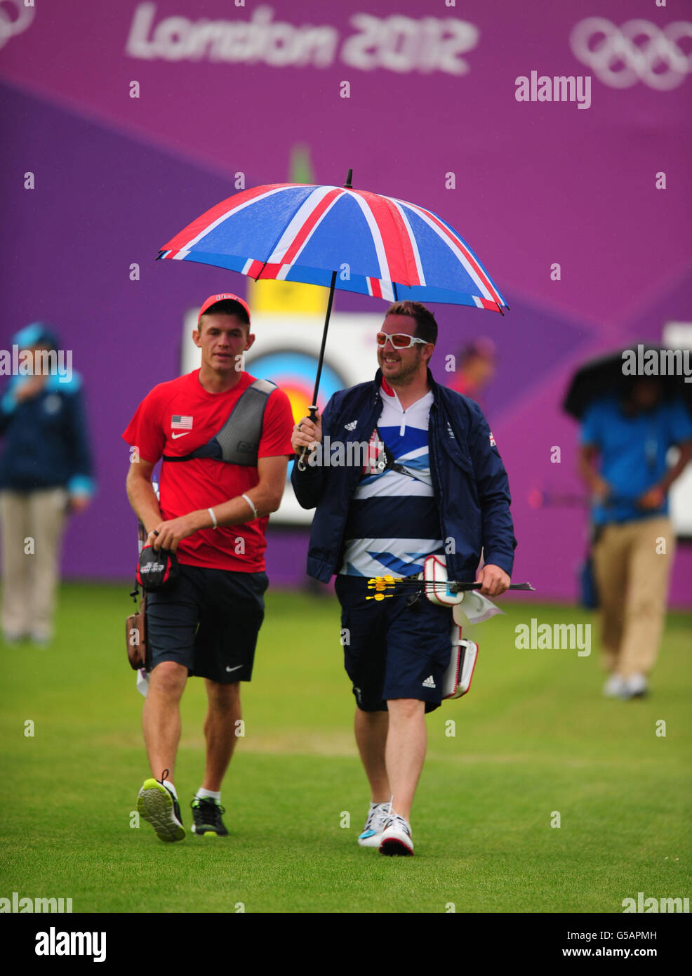 Larry Godfrey de Gran Bretaña (derecha) regresa a su posición de tiro sosteniendo un paraguas con Jacob Wukie de Estados Unidos (izquierda) durante la Ronda de Clasificación de Arqueros individuales de hombres en Cricket Lords Ground, Londres. Foto de stock