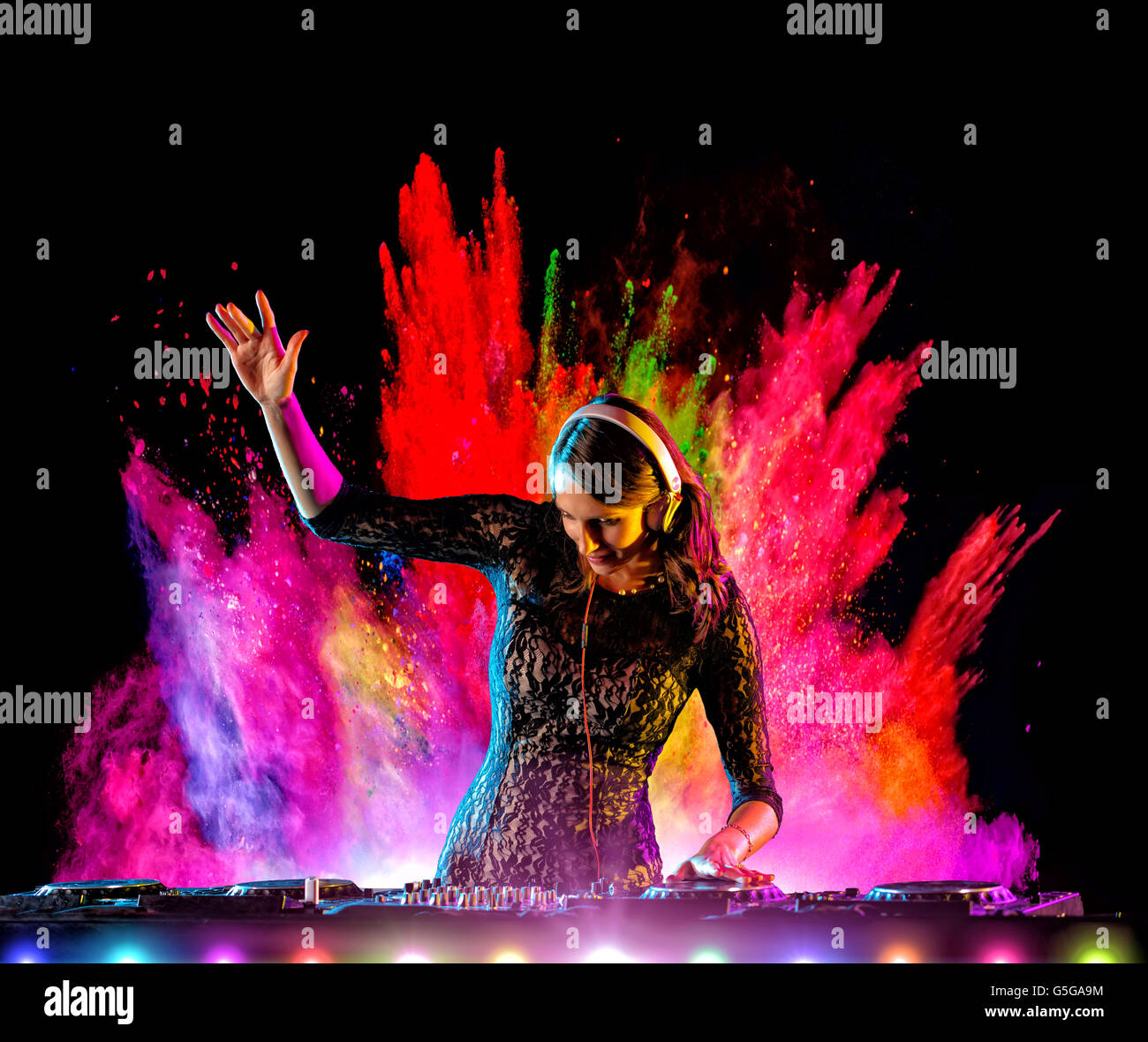 Disc Jockey niña morena mezclando música electrónica con polvo coloreado explosión en fondo Foto de stock