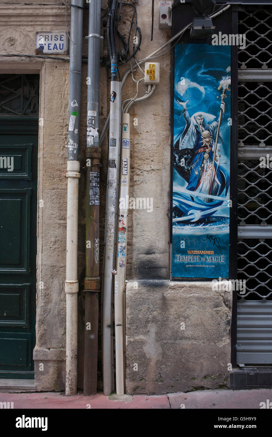 Un póster para juego de fantasía Warhammer junto con los cables de alimentación y caños de desagüe, en una calle lateral de Montpellier, en el sur de Francia. Foto de stock