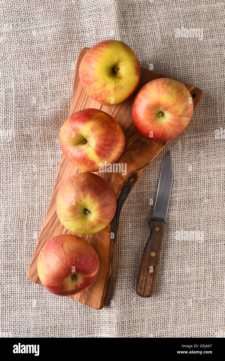 Un alto ángulo de visualización de un grupo de Braeburn manzanas sobre una tabla para cortar, con un cuchillo sobre una tabla de tela de arpillera. Foto de stock