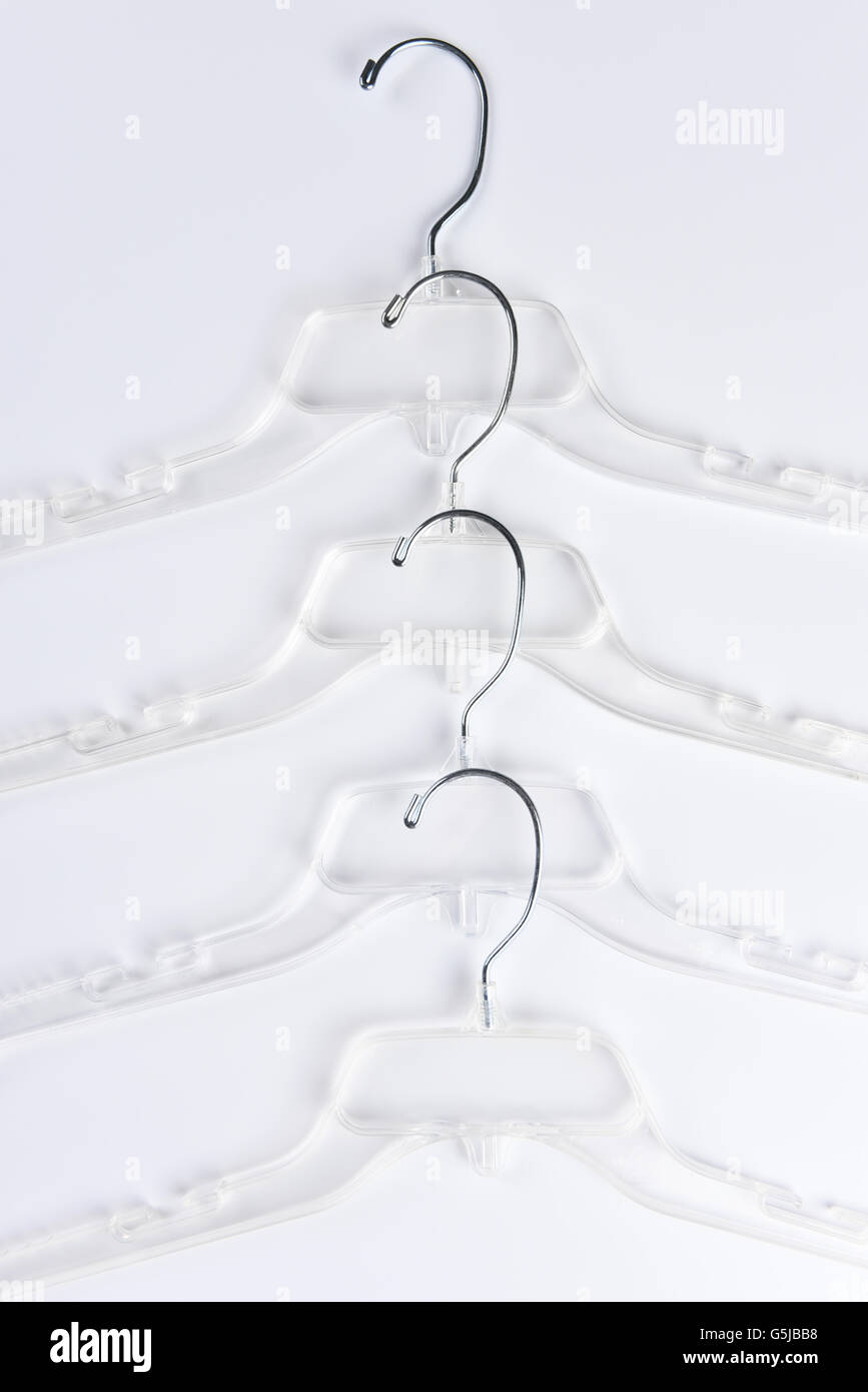 Un alto ángulo de visualización de un grupo de perchas de plástico transparente sobre un fondo blanco, el formato vertical. Foto de stock