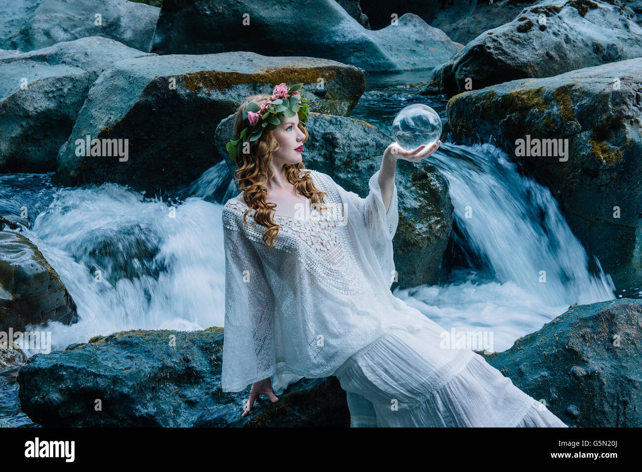 Mujer caucásica sosteniendo la bola de cristal en la cascada del río Foto de stock