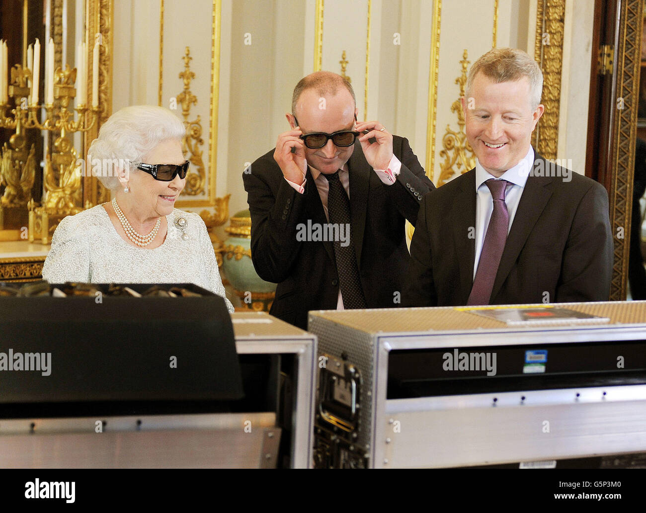 La reina Elizabeth II con el productor John McAndrew y el director John Bennett (derecha), en la sala de dibujo blanca del Palacio de Buckingham en el centro de Londres, mientras observan la grabación de su mensaje navideño a la Commonwealth que se transmitirá por primera vez en 3D. Foto de stock