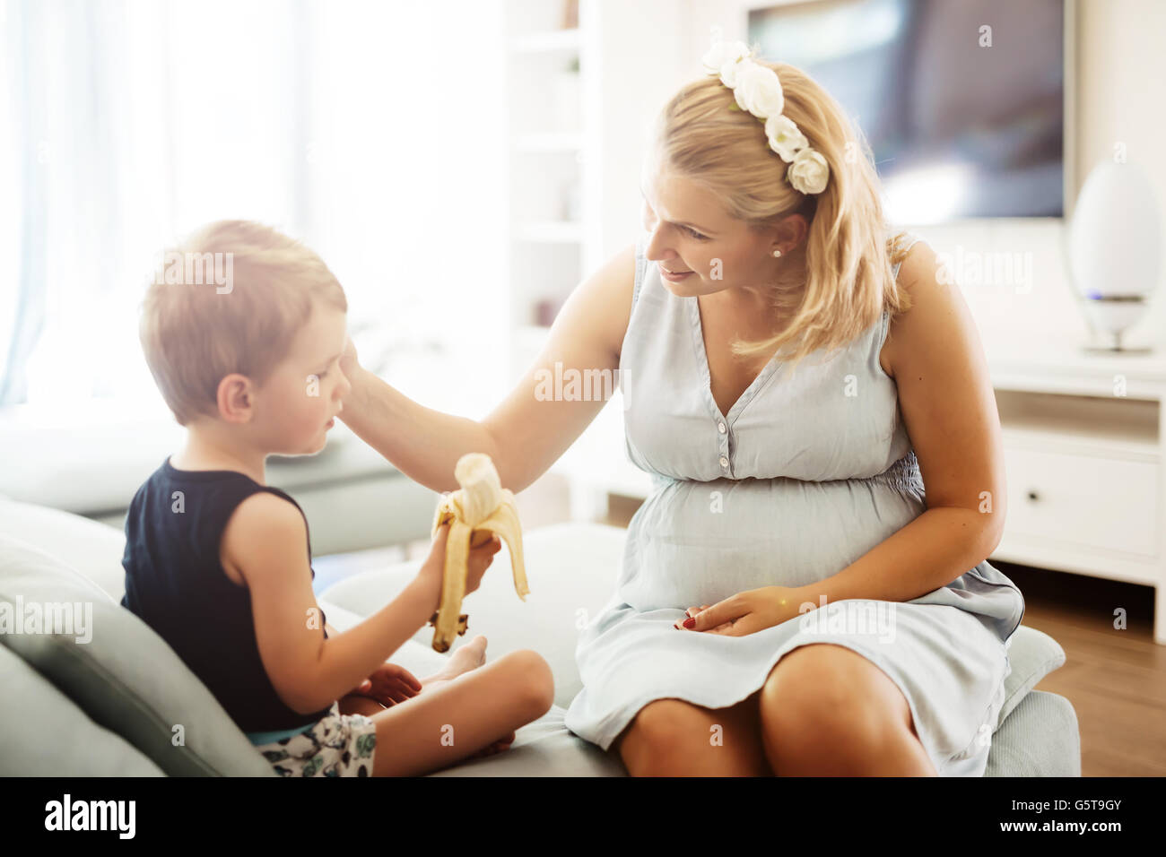 Hermosa madre caricias niño mientras earing un plátano Foto de stock
