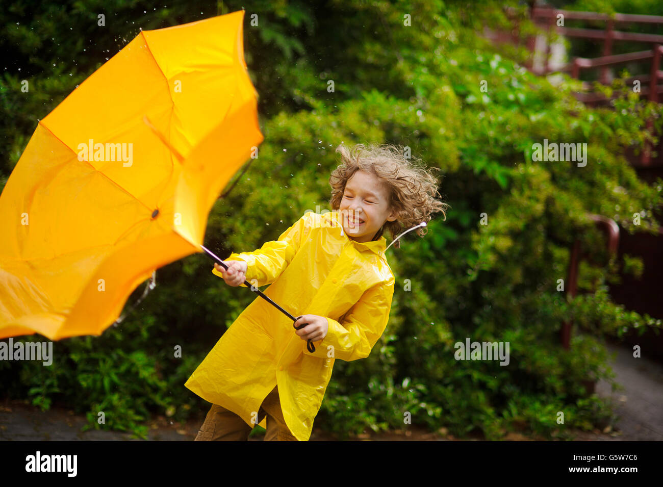El chico en un impermeable amarillo brillante con esfuerzo sostiene un paraguas  contra el viento. El fuerte viento saca un paraguas amarillo desde su ha  Fotografía de stock - Alamy