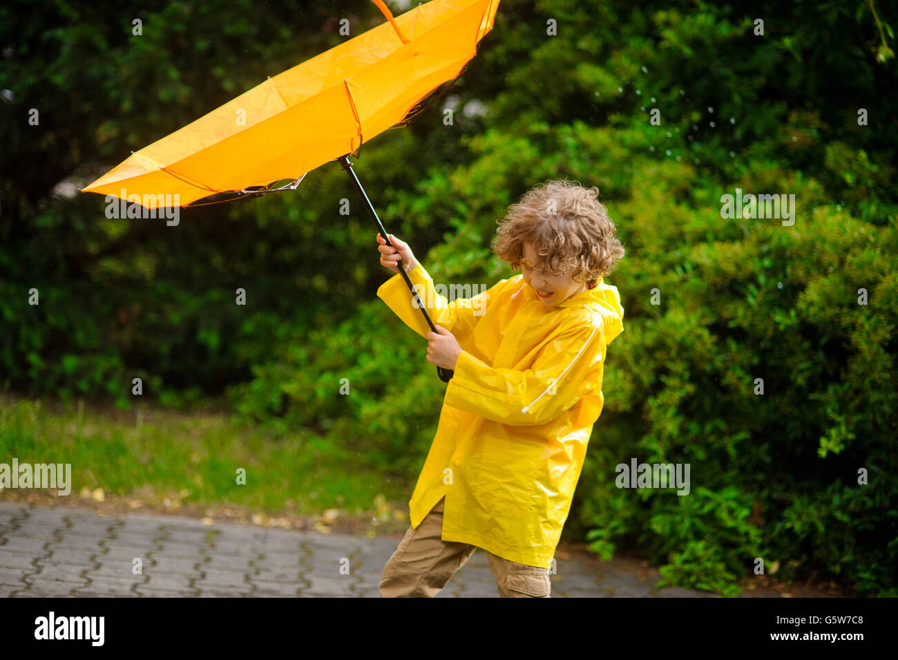 El niño de 8-9 años con esfuerzo sostiene un paraguas de windflaws. Él ha  cerrado los ojos a la tensión e intenta resistir en pie Fotografía de stock  - Alamy