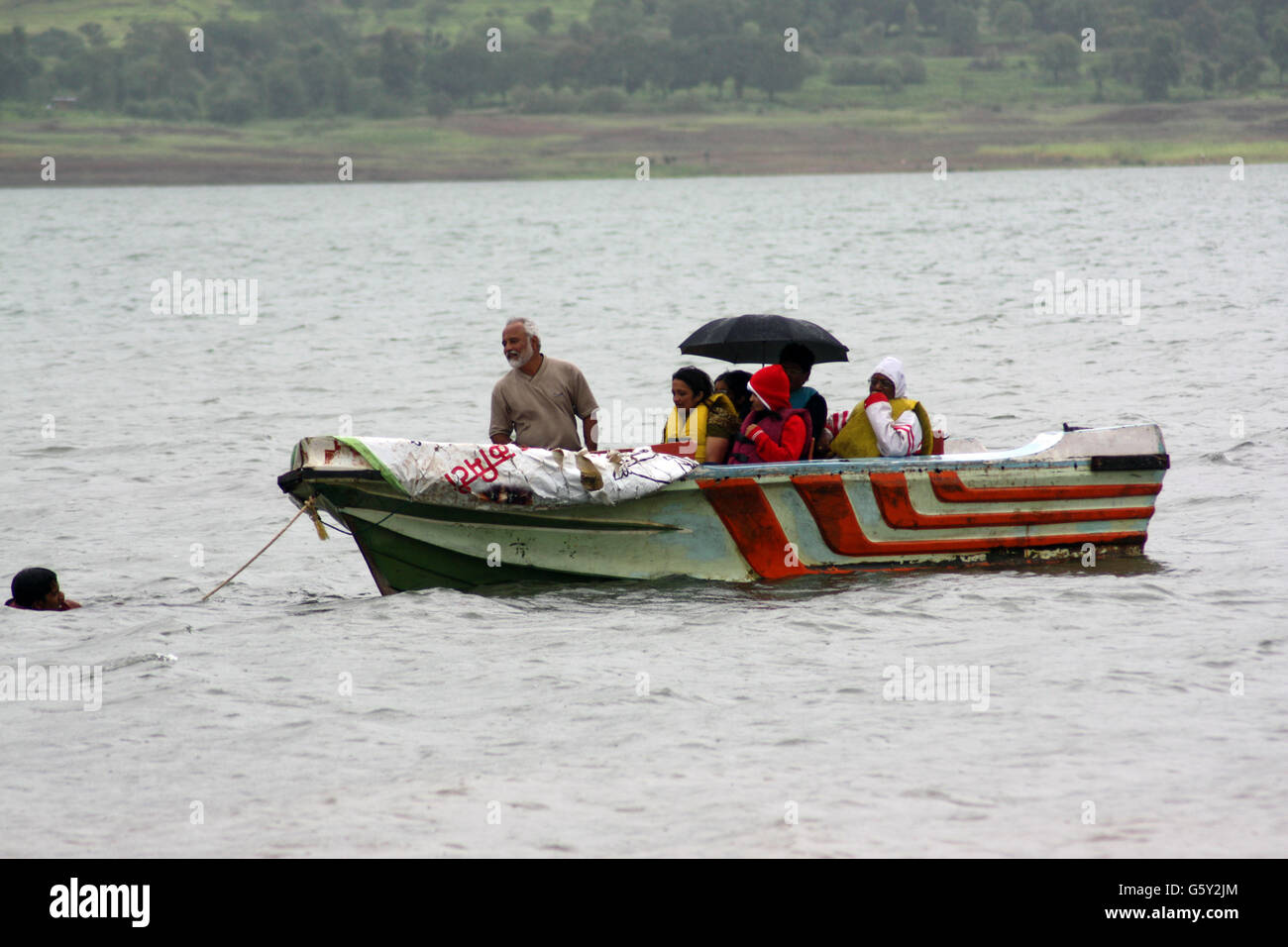 Un trabajador de rescate para sacar un bote de turistas varados en un río inundado en la India. Foto de stock