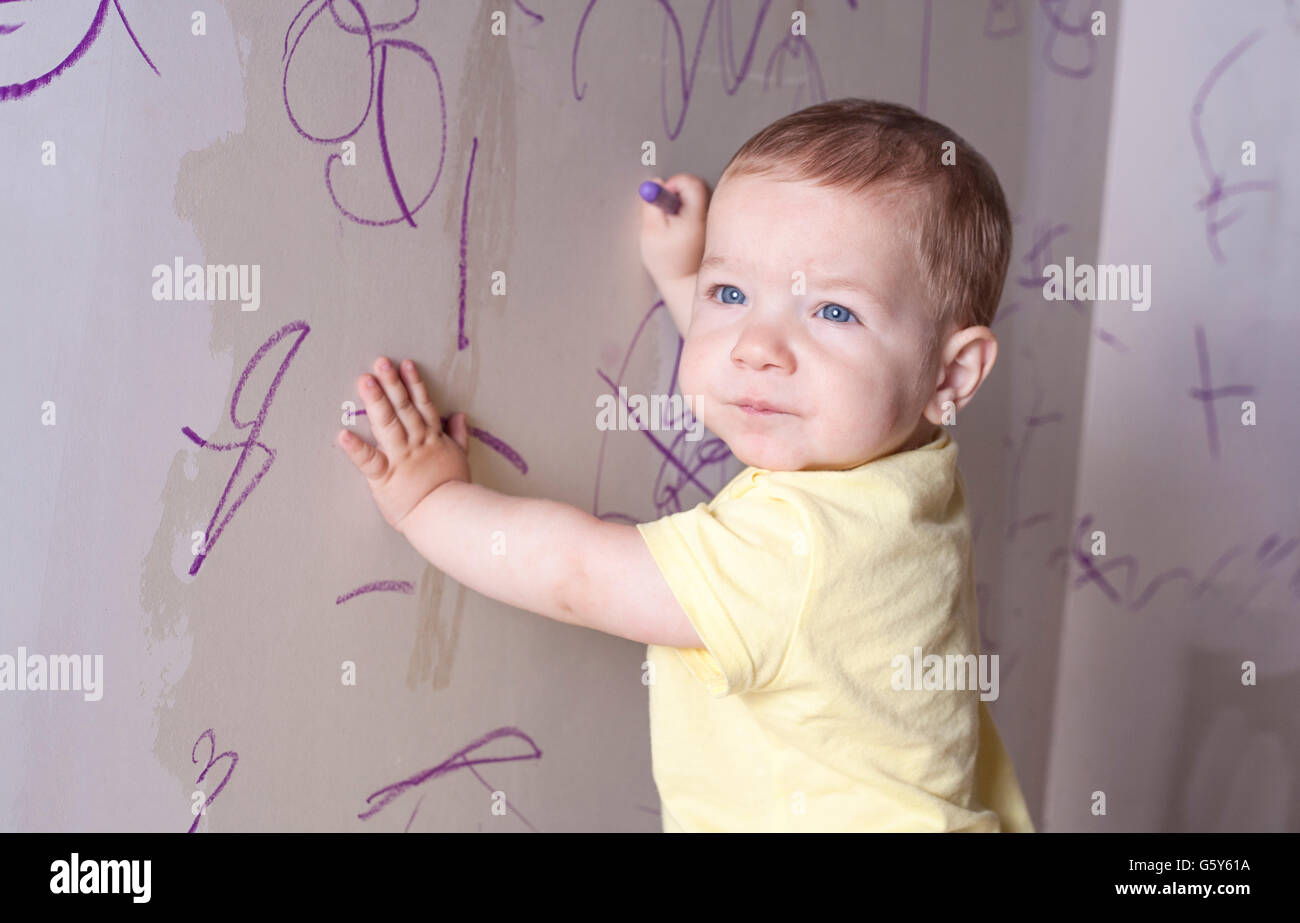 Baby Boy dibujo con lápiz de cera sobre la pared de yeso. Él tiene el