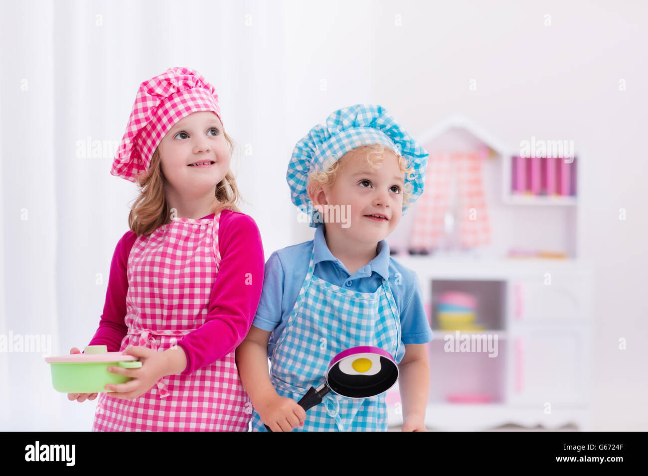 Niña y Niño en el chef hat y delantal Cocinando huevos fritos en una cocina  de juguete. Juguetes de madera para niños pequeños. Los niños juegan y  cocinar Fotografía de stock -