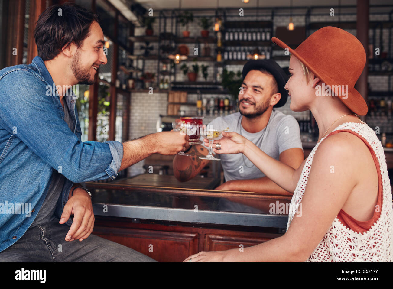 Tres jóvenes bebidas en el café tostado. Los hombres jóvenes y una mujer con una copa en el bar. Foto de stock