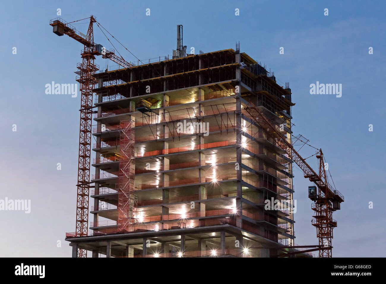 Edificio de hormigón de gran altura con grúas de construcción en penumbra Foto de stock