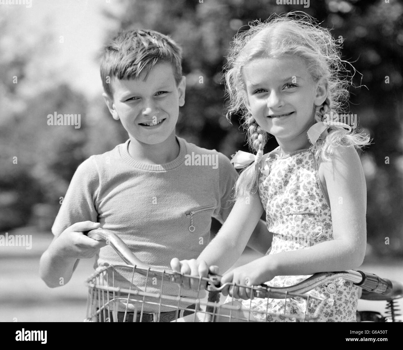 1930 1940 Retrato sonriente niño empujando MOTO CON LA CHICA RUBIA PIGTAILS sentado por el manillar tanto mirando a la cámara Foto de stock