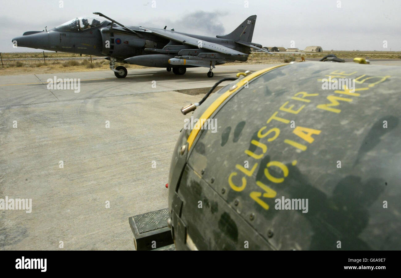 Royal Air Force Harrier Británico GR7 taxis pasando un carro de bombas de racimo antes de ser cargados en su base en Kuwait. Estados Unidos admite que los ha utilizado en Iraq; Gran Bretaña dice que los tiene, pero no los utilizaría en zonas edificada. *... Irak dice que han matado a docenas de civiles; y los grupos de derechos humanos insisten en que deben ser prohibidos. Las bombas de racimo son mortales pero impredecibles - cada una contiene más de 200 bomblets del tamaño de una lata de bebidas que se dispersan sobre un área del tamaño de dos campos de fútbol, la mayoría de explosión en el impacto y capaz de rasgar a través de cuarto de pulgada de acero. Foto de stock