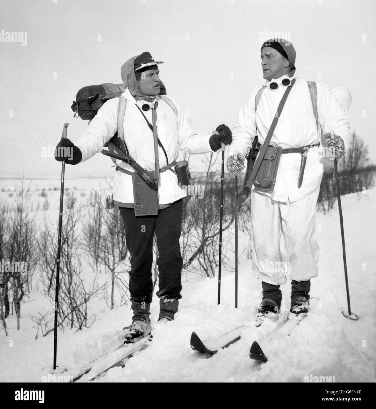 Los actores Richard Harris (izquierda) y Kirk Douglas se arzan a través de la nieve pesada en Noruega, mientras que en el lugar para la película de guerra Los Héroes de Telemark. Foto de stock