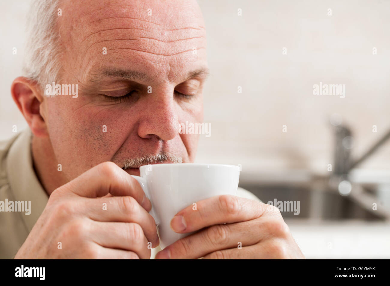 Cerrar el único hombre maduro barbudo con ojos cerrados y expresión soñolienta tomando café desde la pequeña taza de té blanco Foto de stock