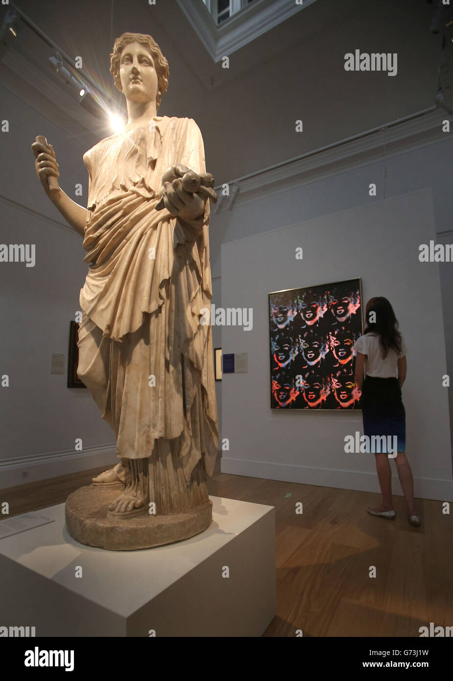 Una estatua de mármol de Aphrodite de principios del siglo 1st dC (la venta es de 4-£6 millones de libras) mientras un visitante mira 'Nine Multicolored Marilyns' (serie de reversión) de Andy Warhol (la venta es de 4-£6 millones de libras) detrás, en el verano en Sotheby's, magnífica exposición de Obras en Londres, que lanza su temporada de subastas de verano. Foto de stock