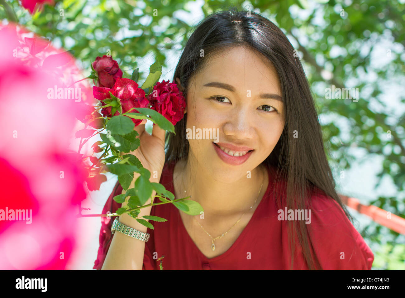 Mujer de vestido rojo, sosteniendo una rosa roja cerca de su rostro Foto de stock