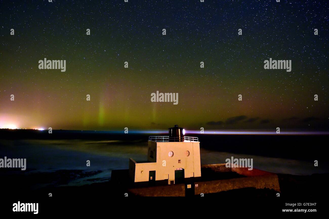 Nota de los editores: Fotografía tomada con una exposición larga. Una aurora se ve en el horizonte detrás del faro de Bamburgh en Northumberland. Foto de stock