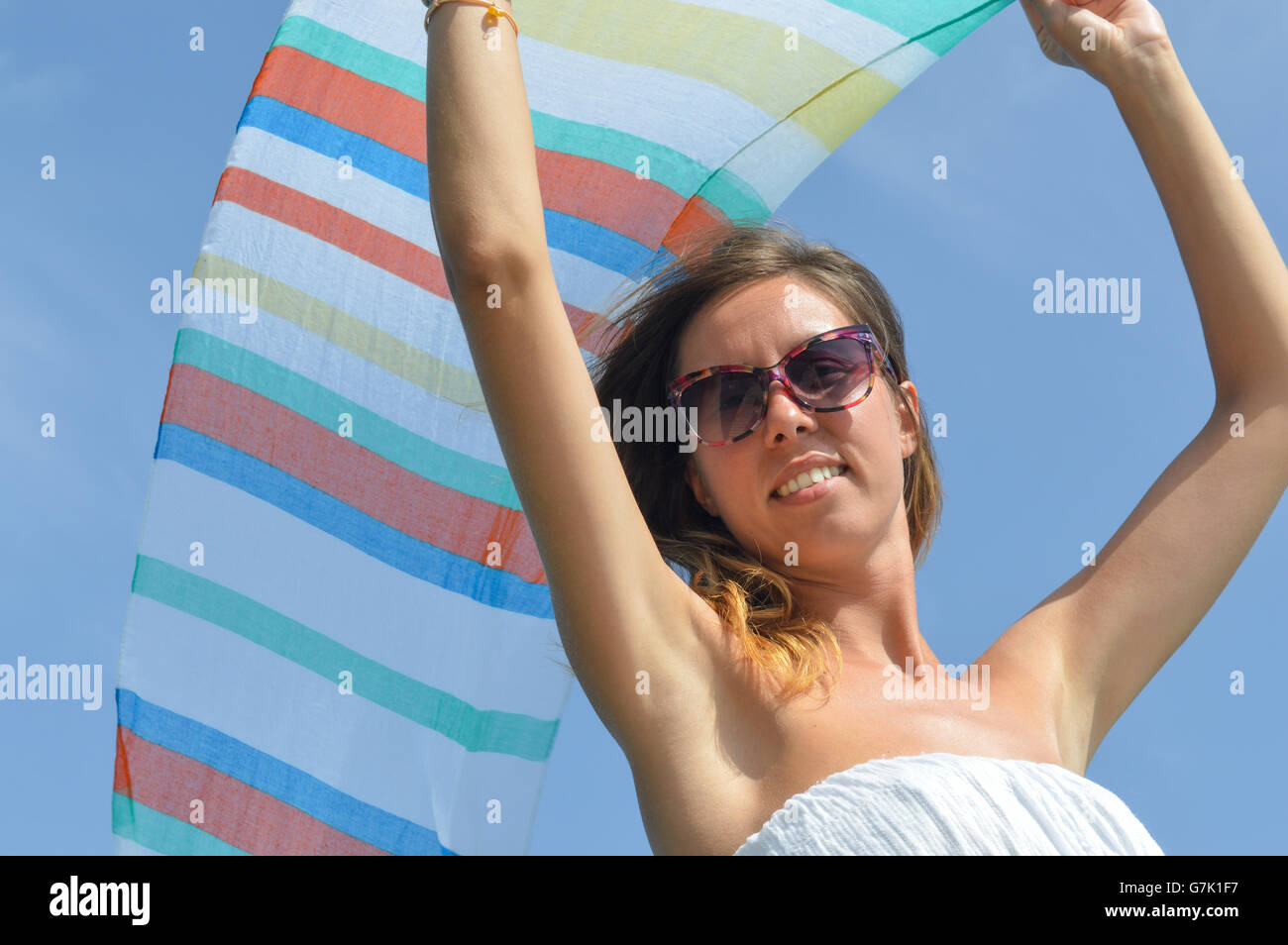 Chica agitando una colorida bufanda en seaside contra el cielo azul Foto de stock
