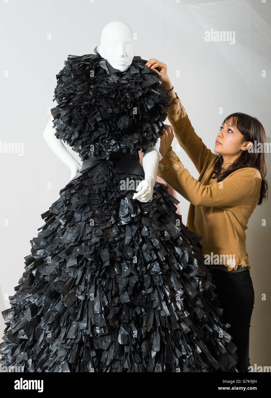 Angela Tye ajusta un vestido Gareth Pugh usado por Lady Gaga, que está hecho de bolsas de basura negras trituradas, parte de la exposición "Women Fashion Power" en el Design Museum, Londres, que examina cómo las mujeres influyentes en la política, los negocios y la cultura popular han utilizado e influido en la moda. Foto de stock
