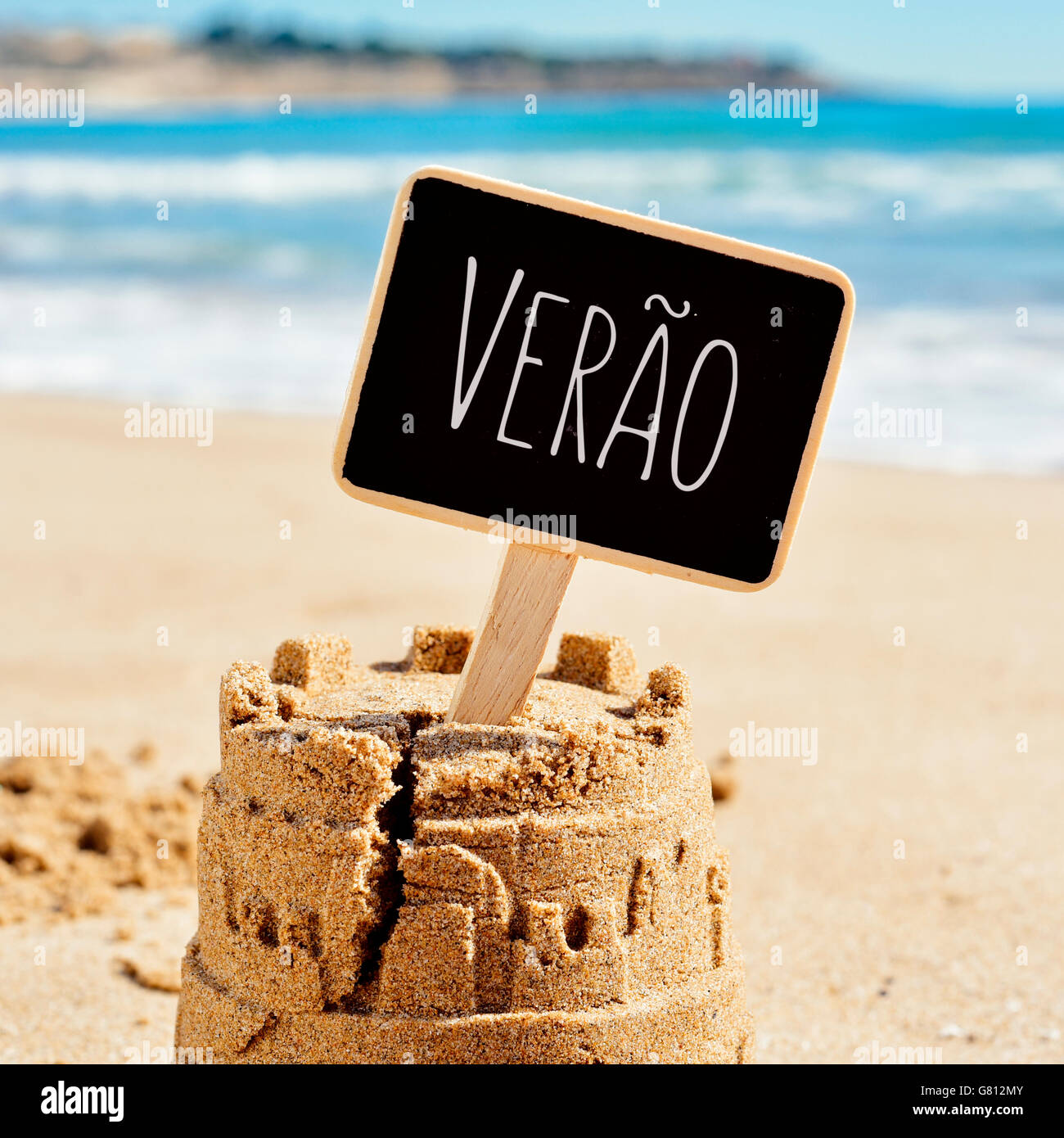 Primer plano de un castillo de arena en la arena de una playa negra rematada con un cartel con el texto verao, verano en portugués escrito, yo Foto de stock
