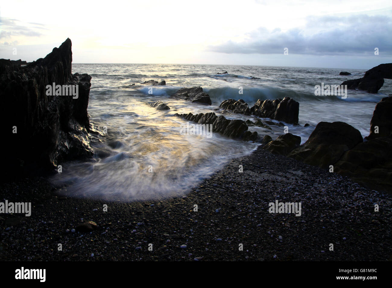 Siluetas de piedras irregulares en una orilla infiltrado con una espuma de mar como olas curl en la playa Foto de stock