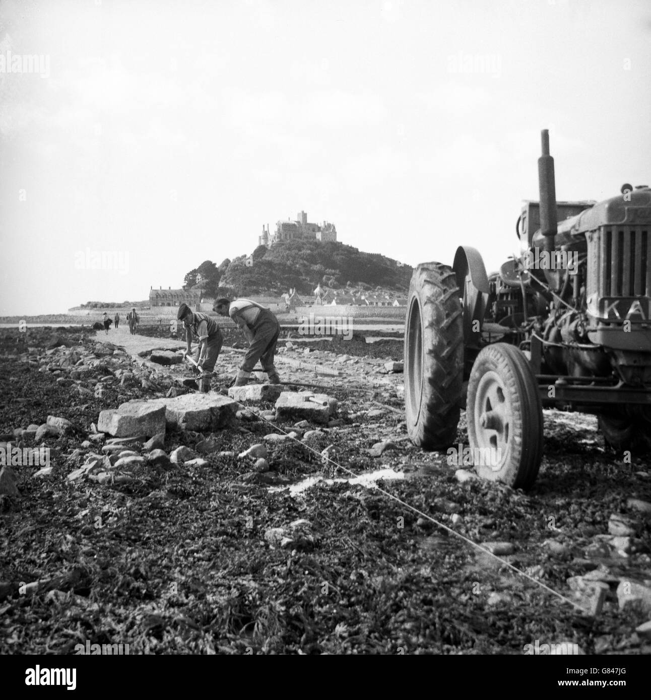 Obreros reparando la antigua carretera de piedra que conduce al Monte de San Miguel en Cornwall, que solo está expuesto en marea baja. Foto de stock