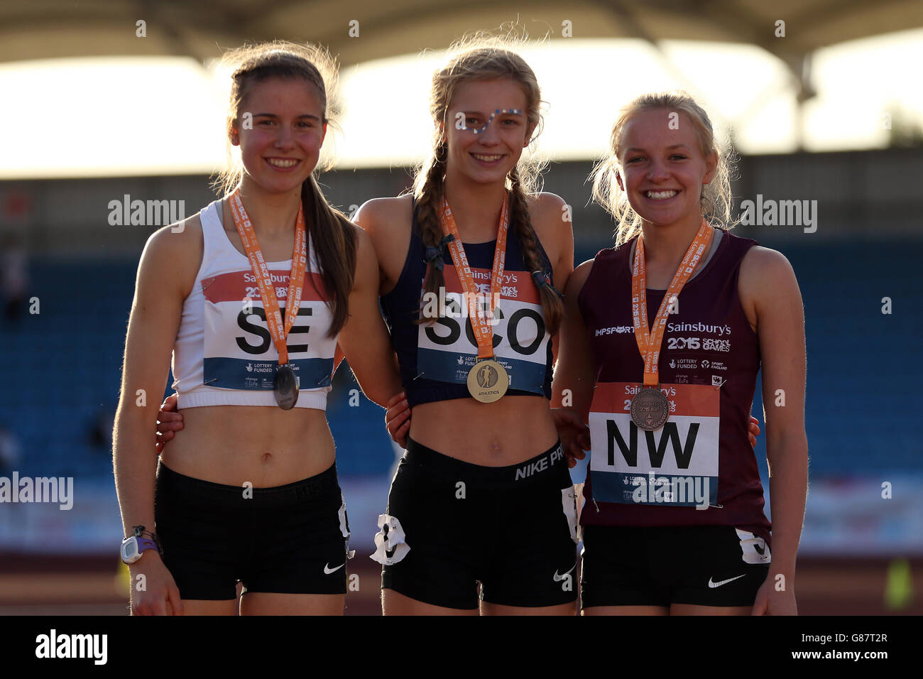 (l-r) Chloe Sharp, de Inglaterra del sudeste, Erin Wallace, de Escocia, y Katie Lowery, de Inglaterra del noroeste, reciben sus medallas de 1500m durante la ceremonia de la medalla en los Juegos escolares de Sainsbury 2015 en el Manchester Regional Arena. Foto de stock