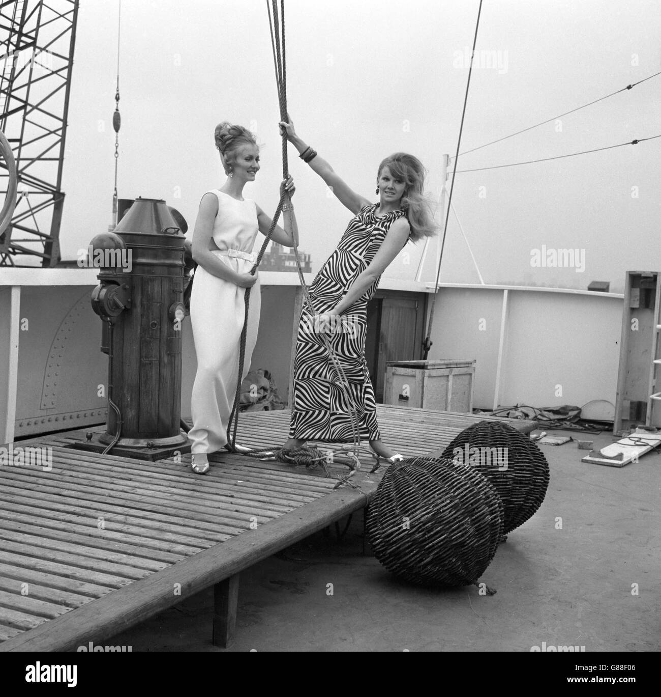 El modelo Nikki Ross (izquierda) lleva un vestido blanco por la noche de Frederick Starke, mientras que Virginia Bird lleva una creación en blanco y negro de Frank Usher, mientras se posan a bordo del carguero Benarmin en Victoria Dock, Londres. Ambos se mostrarán en la próxima Semana Británica en Hong Kong. Foto de stock