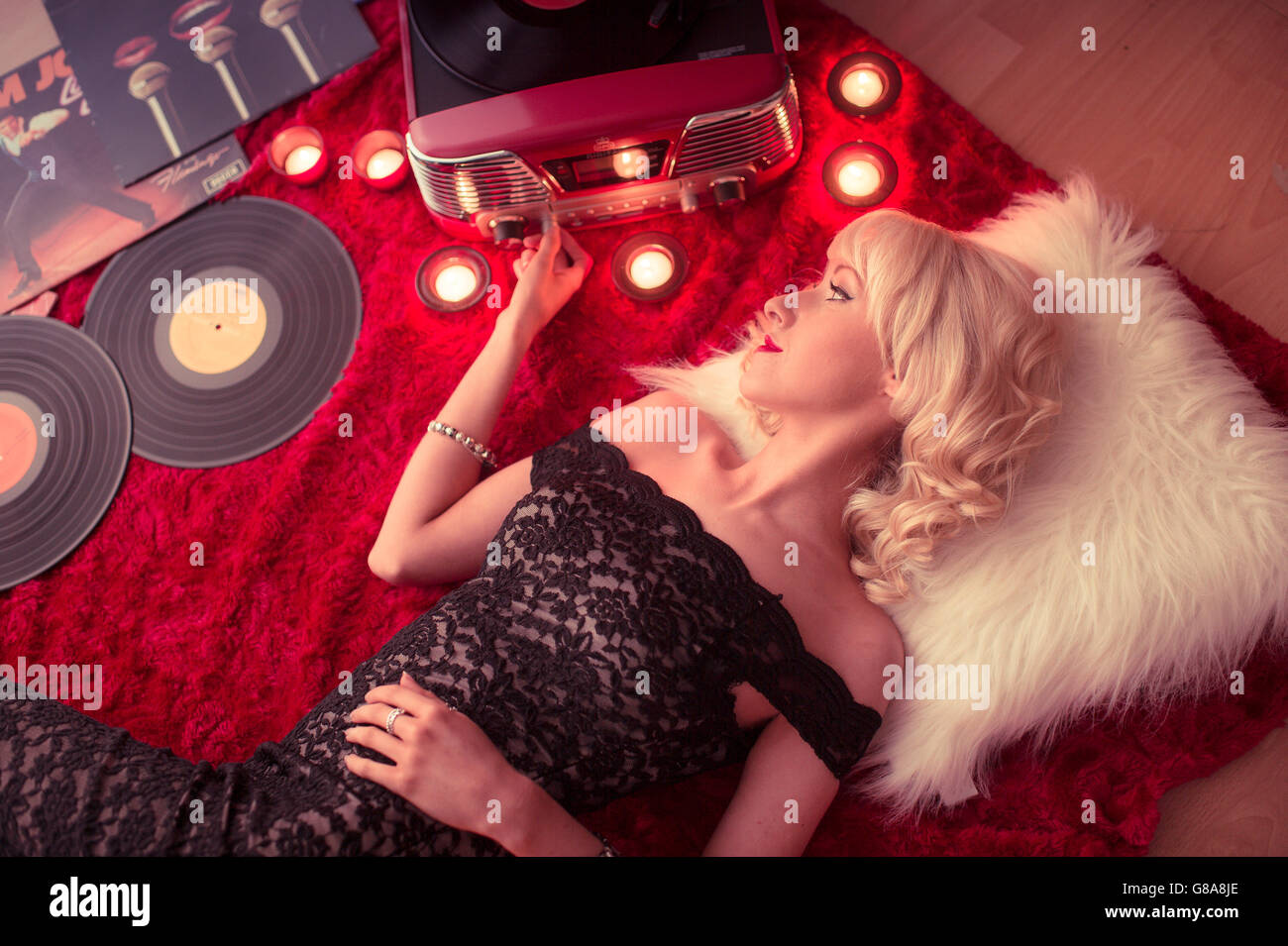 Retro chic de los 50's: una joven mujer rubia chica acostada en el suelo escuchando música en vinilo analógico álbumes LPs registros dispersos en el piso en casa UK Foto de stock