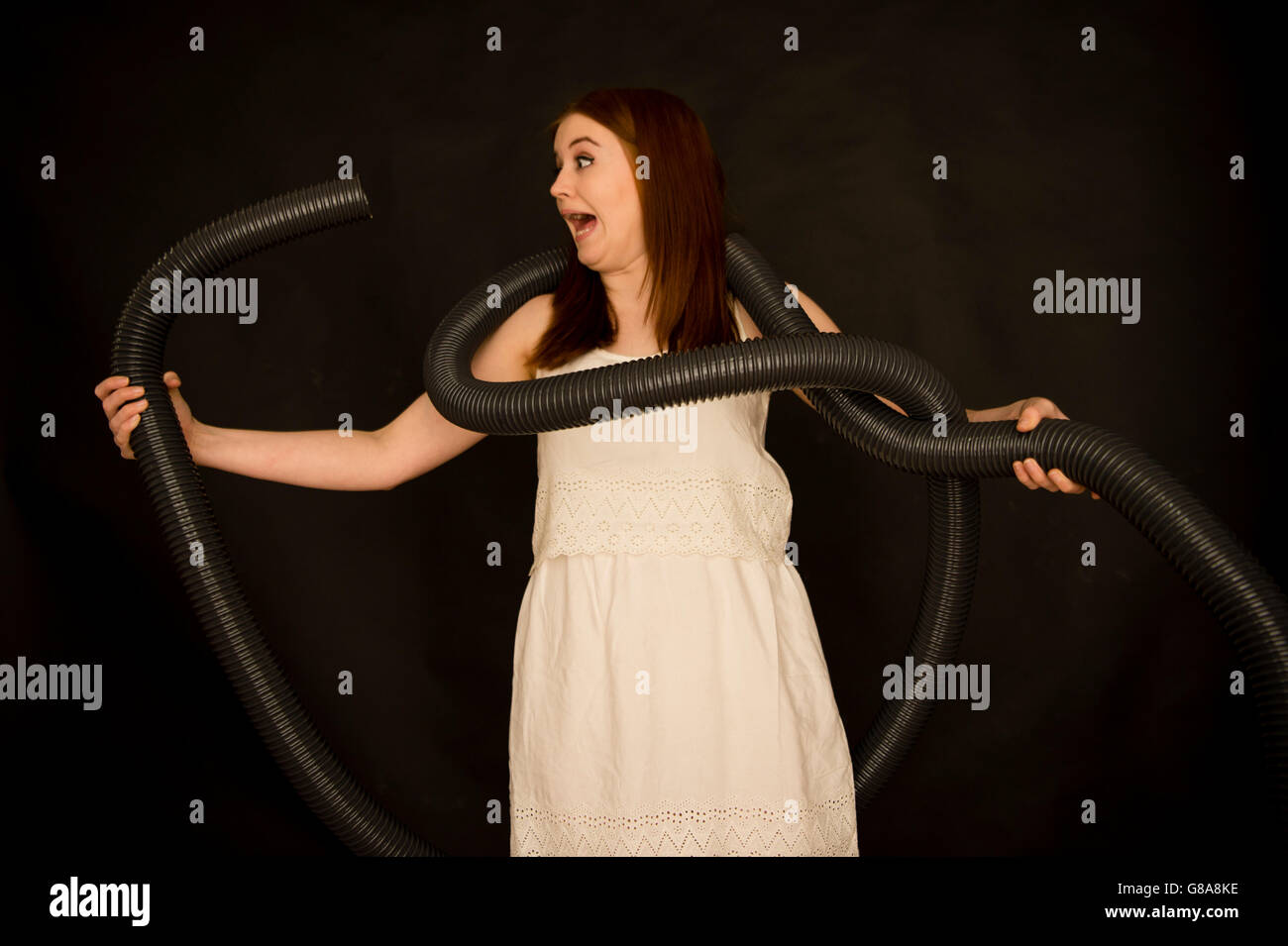 Una mujer joven en un vestido blanco luchando con bobinas de tubo plástico largo como una serpiente serpiente , buscando confundir miedo preocupado abrumada, UK Foto de stock