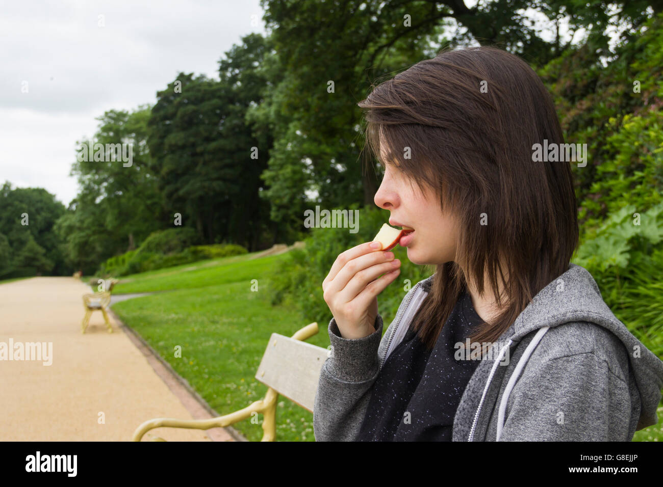 Mujer joven, adulto o el final de su adolescencia, sentado en el parque comiendo un trozo de manzana. Foto de stock