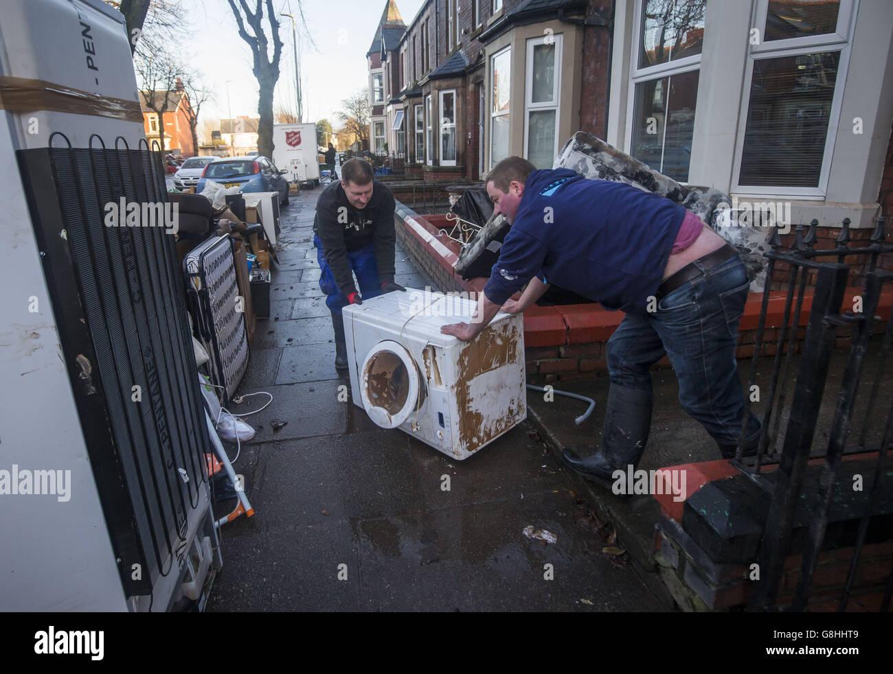 Los hombres sacan un aparato doméstico de una casa mientras la limpieza continúa después de las inundaciones en Carlisle, Cumbria. Foto de stock