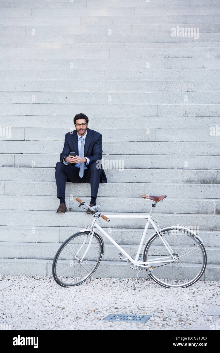 Empresario con bicicleta utilizando el teléfono en la ciudad Foto de stock