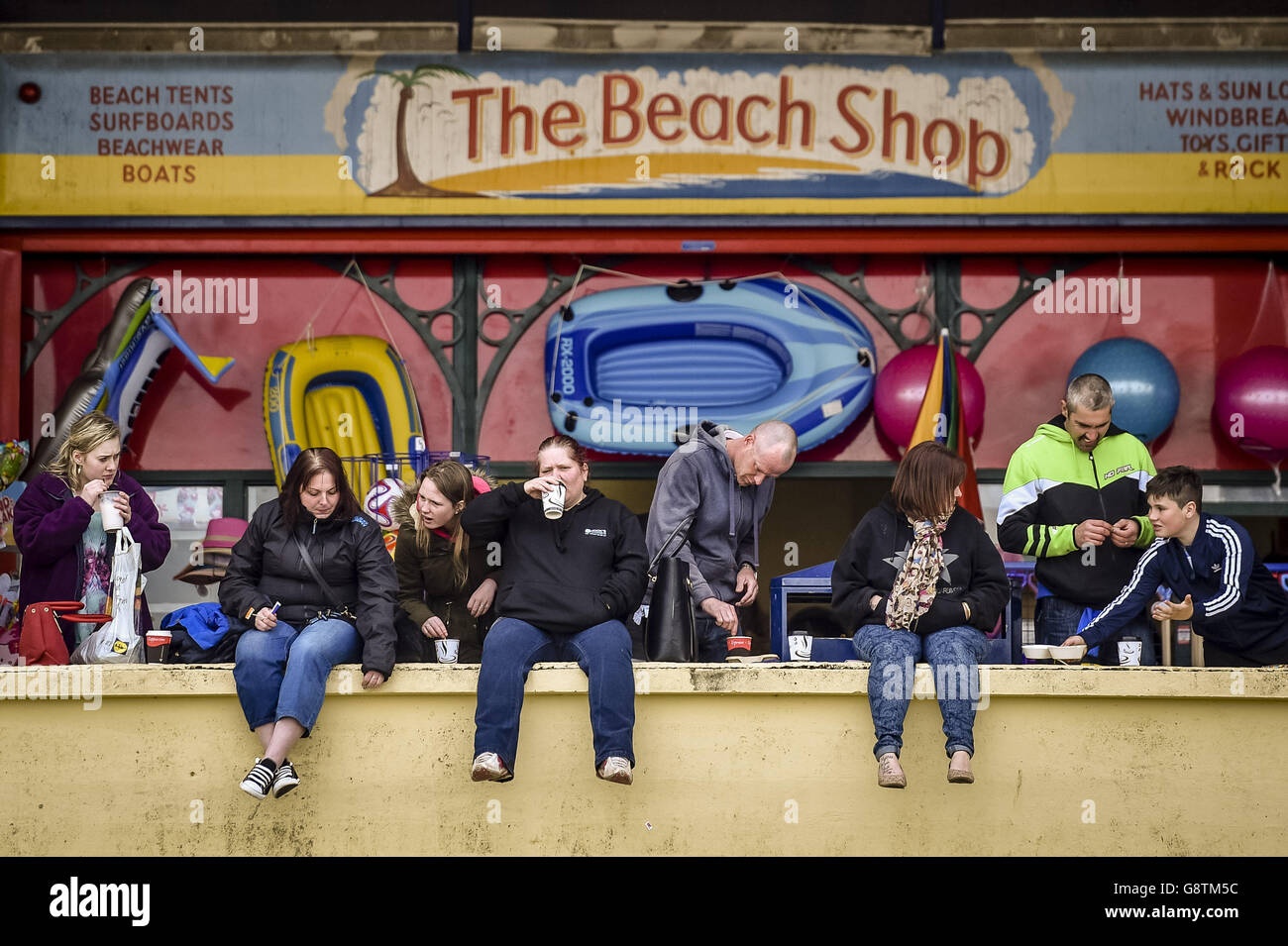 La gente usa chaquetas y toma bebidas calientes en Barry Island, Gales, donde el clima es nublado y aburrido. Foto de stock