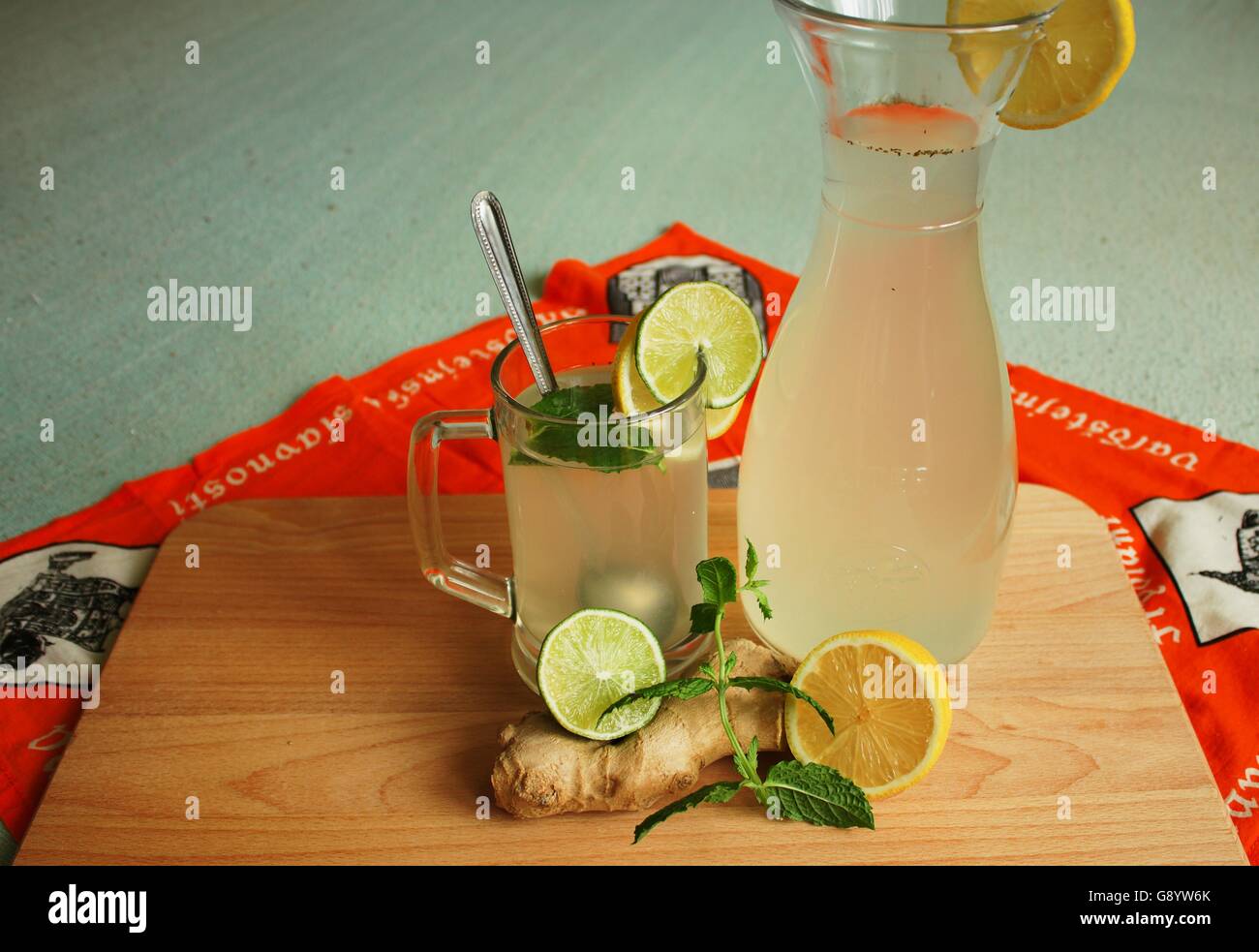 El jengibre y el zumo de limón en una jarra de vidrio y plank jengibre, limón, lima y hojas de menta sobre un fondo de color Foto de stock