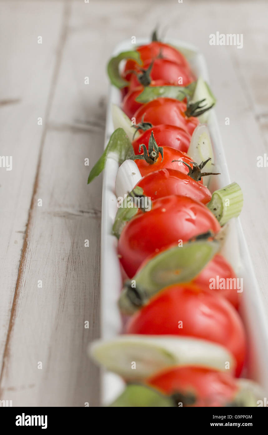 Plato alargado blanco rellena con tomates cherry, cebolla y pimienta Foto de stock