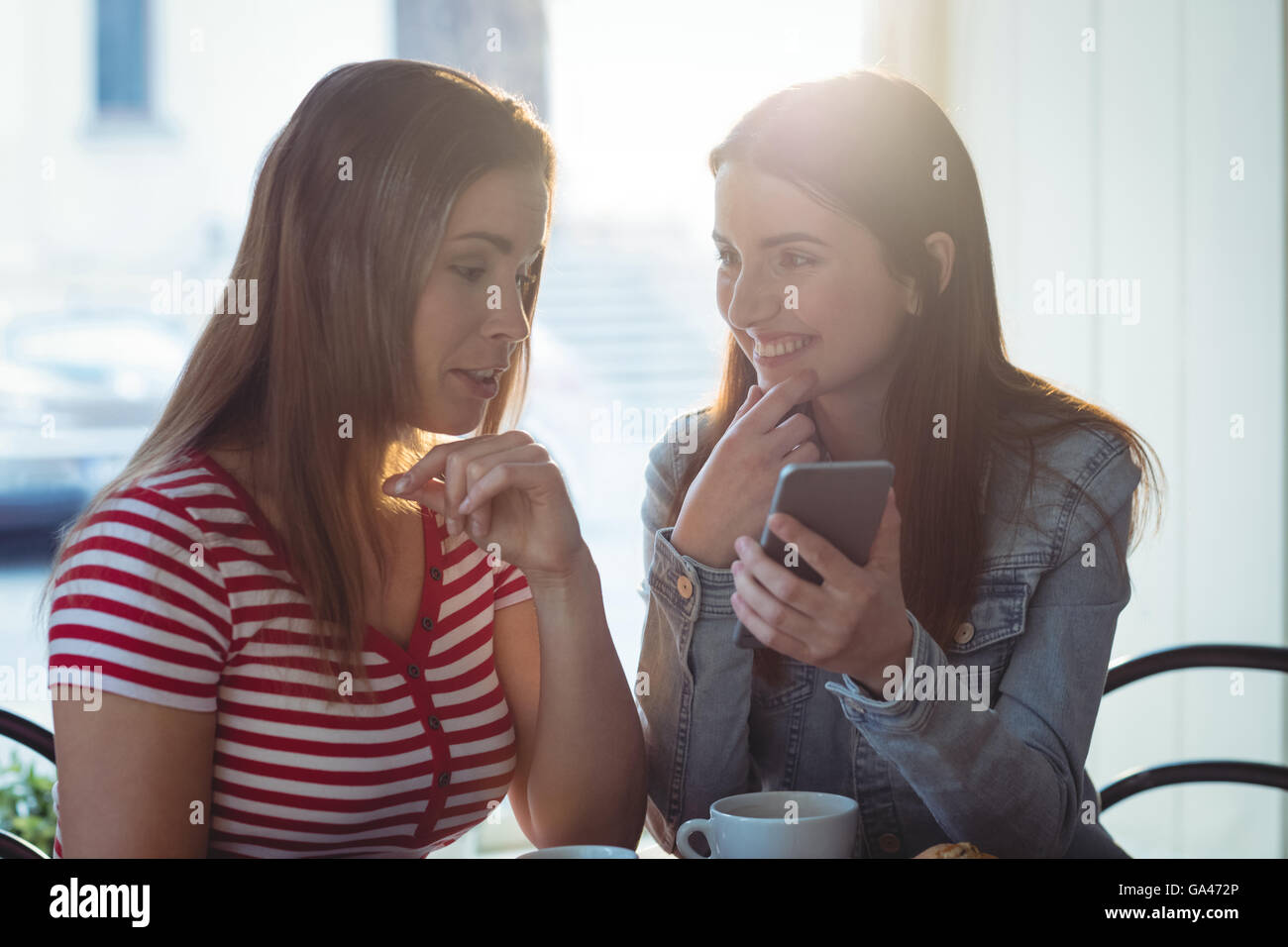 Mujer feliz mostrando celular a un amigo en el café Foto de stock