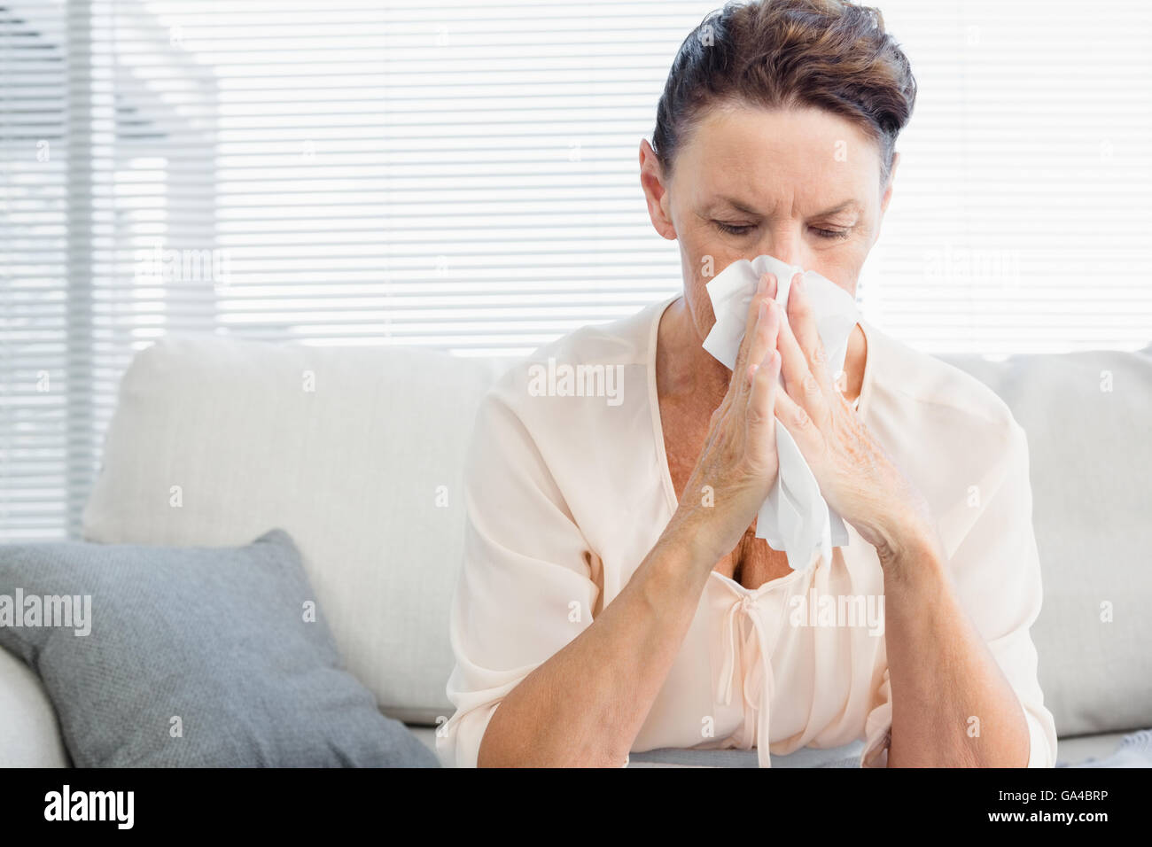 Mujer madura, sufriendo de frío mientras está sentado en el sofá Foto de stock