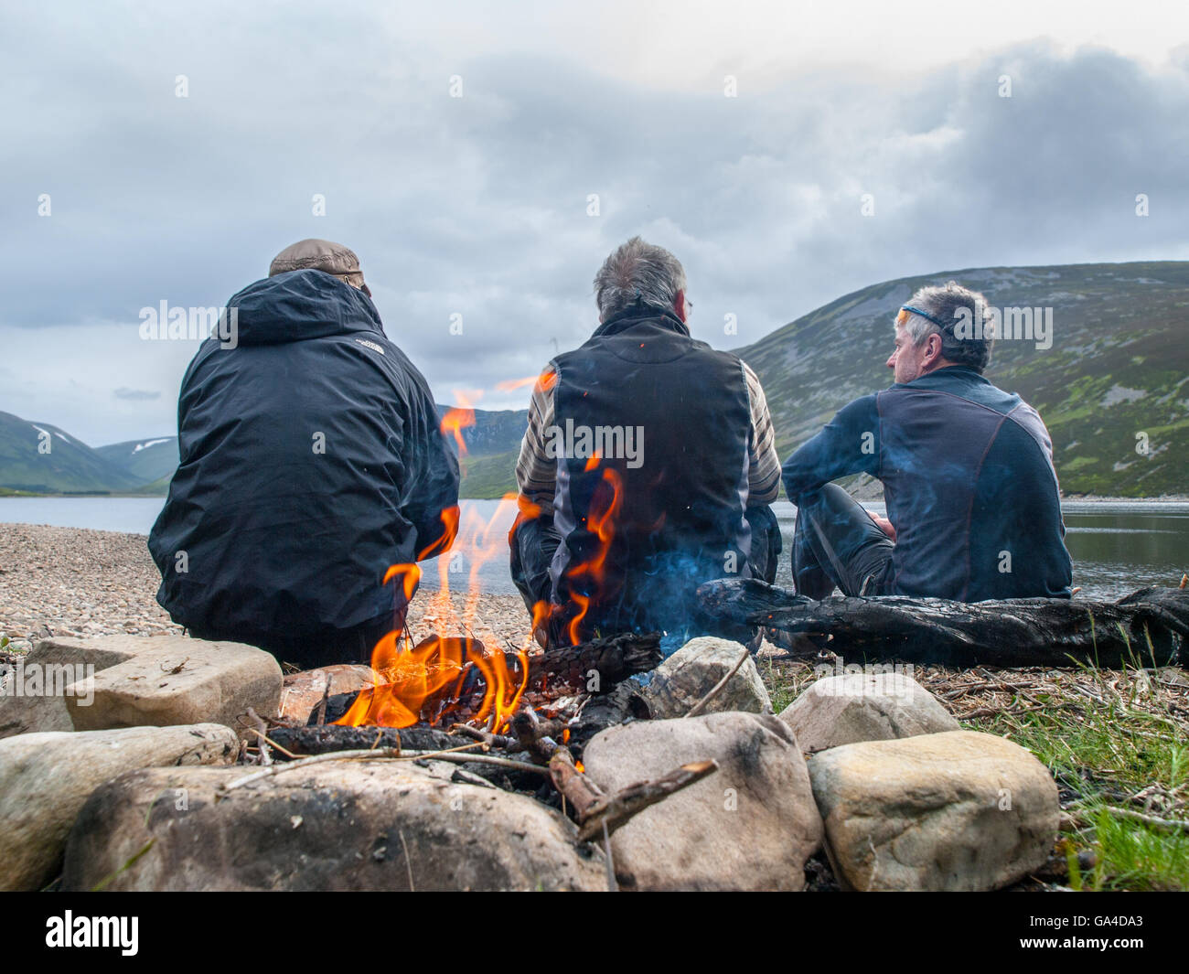 Tres hombres de espaldas a un fuego de campamento en una bicicleta-packing viaje en Escocia Foto de stock