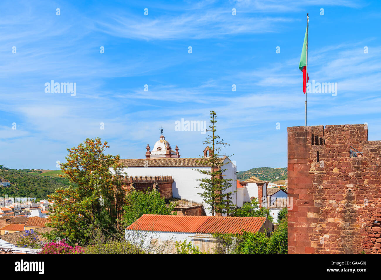 Vista de la torre de castillo con bandera portuguesa y el edificio de la catedral de Silves, ciudad de la región de Algarve, Portugal Foto de stock